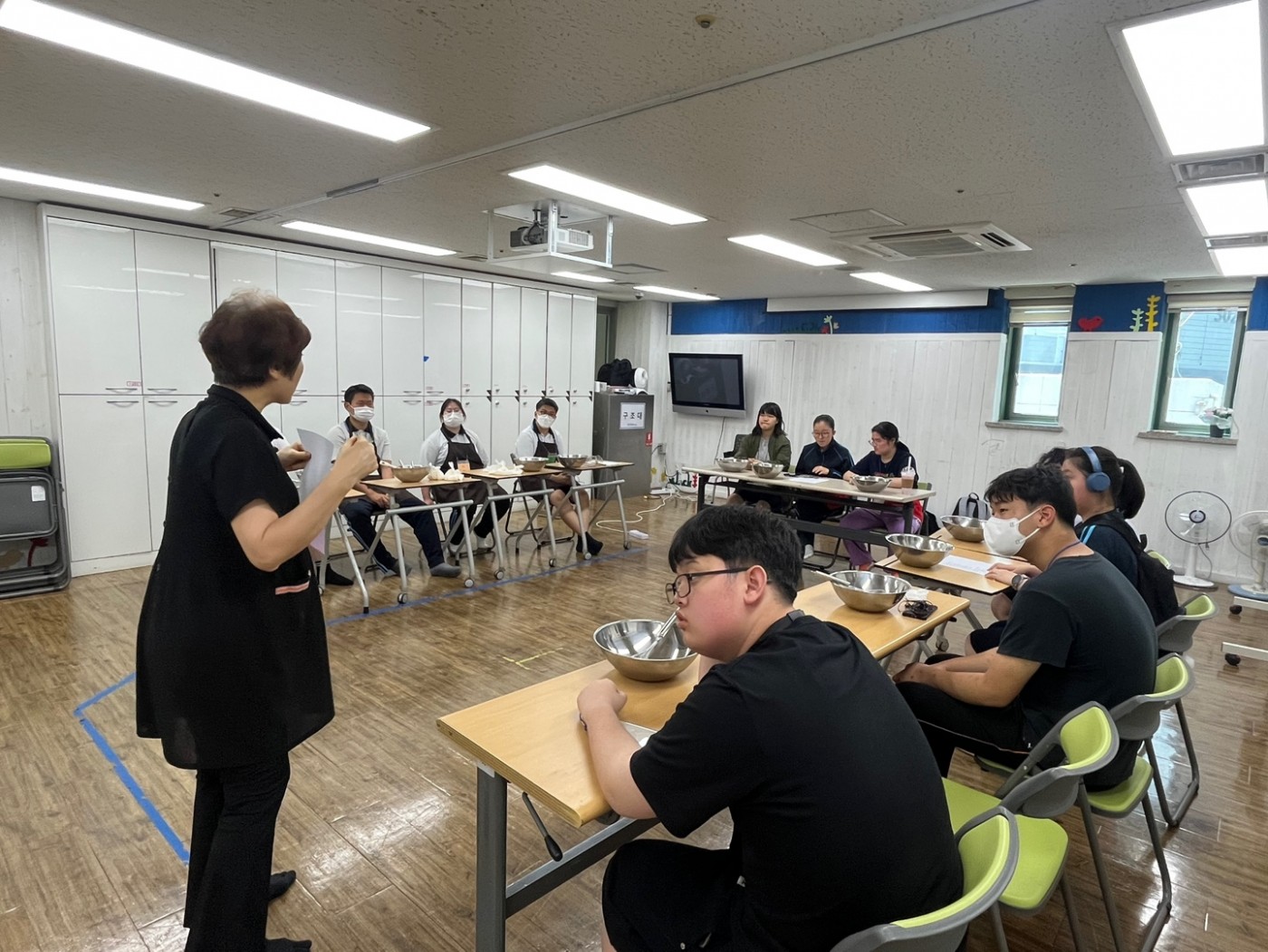 강사가 마들렌 재료를 설명하고 학생들이 집중하여 듣는 모습